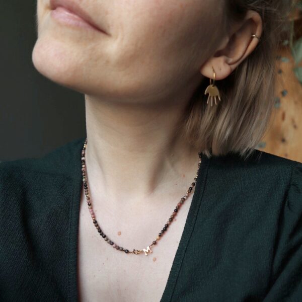 Model met gouden oorbellen met handjes en ketting met rhodoniet.