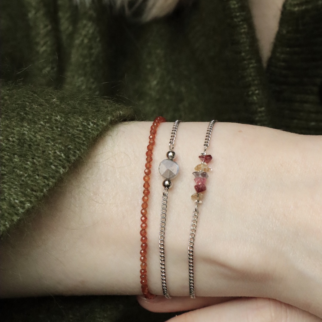 een pols met drie zilveren armbanden. Kralenarmband Dottie met oranje granaat, schakelarmband Mira met labradoriet en schakelarmband Moxie met saffier.