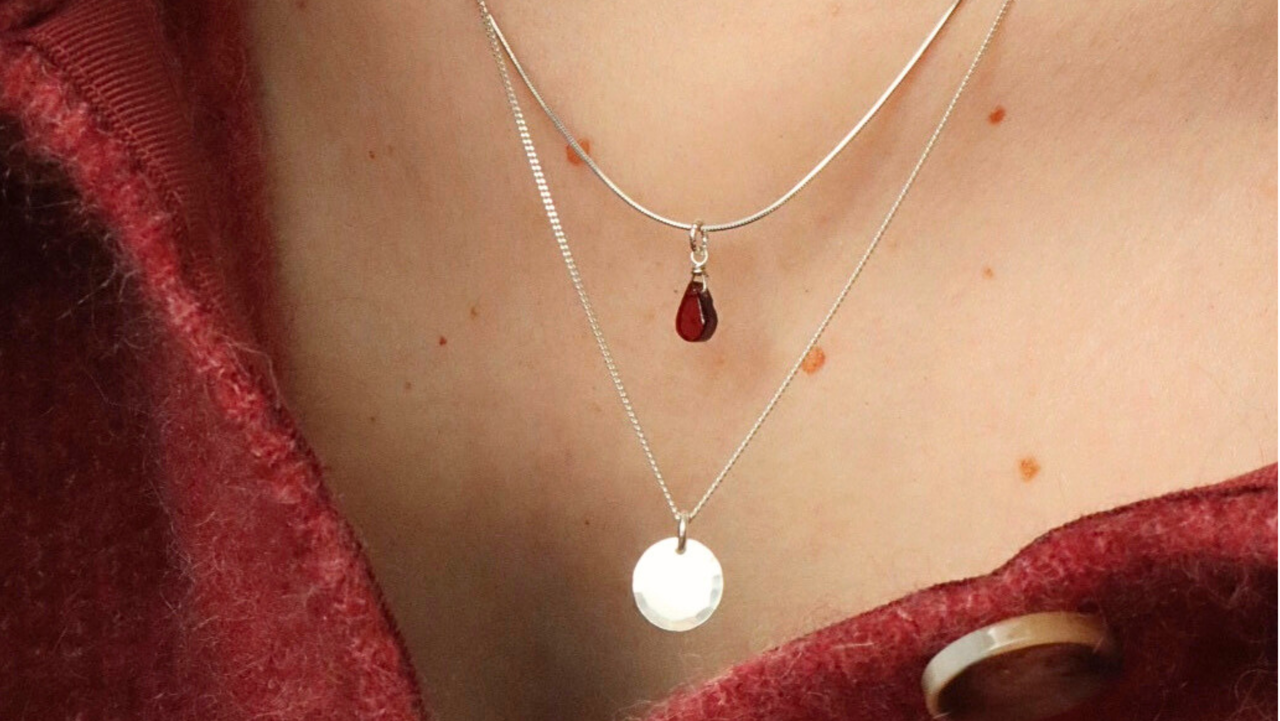Een nek met twee Sterling zilveren kettingen. Eentje met een hanger in de vorm van een druppel van rood granaat en de ander heeft een ronde hanger.